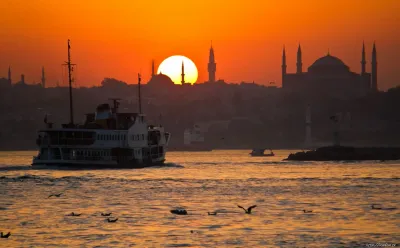 A wooden cruise boat sailing the Bosphorus with the skyline lit by sunset